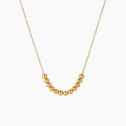 Delicate gold-plated necklace with graduated spherical beads forming gentle smile curve on beige background